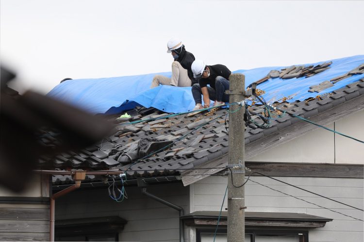 壊れた屋根にブルーシートを掛ける（イメージ、時事通信フォト）