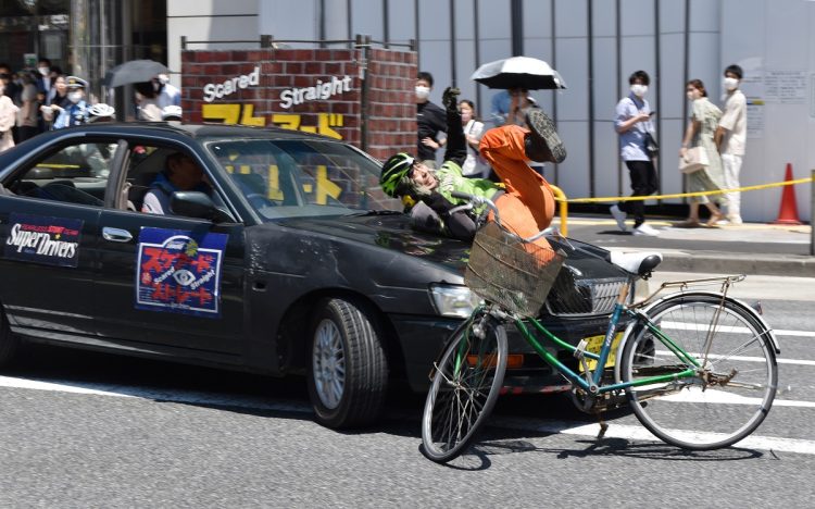 ヘッドホンをしたまま自転車に乗るスタントマンが車に気付かず事故が起きる様子などを再現した交通安全教室（時事通信フォト）