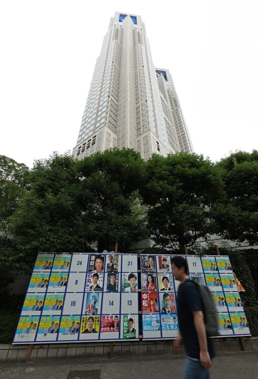 東京都知事選挙が告示され、選挙ポスターが張られた掲示板（下）と都庁。用意された48枠では足りず、49以降の候補者は自分で枠外に貼ることとなった（時事通信フォト）
