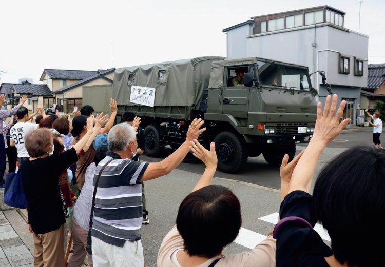 「ありがとう」と声を上げて車両を見送る住民たち